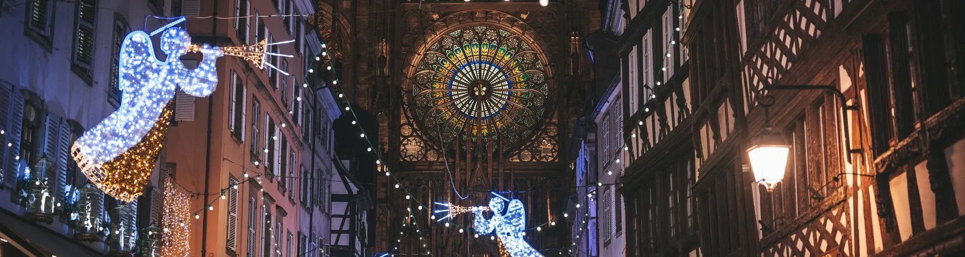 Rue décorée avec illuminations d'anges bleus et dorés, cathédrale gothique illuminée en arrière-plan