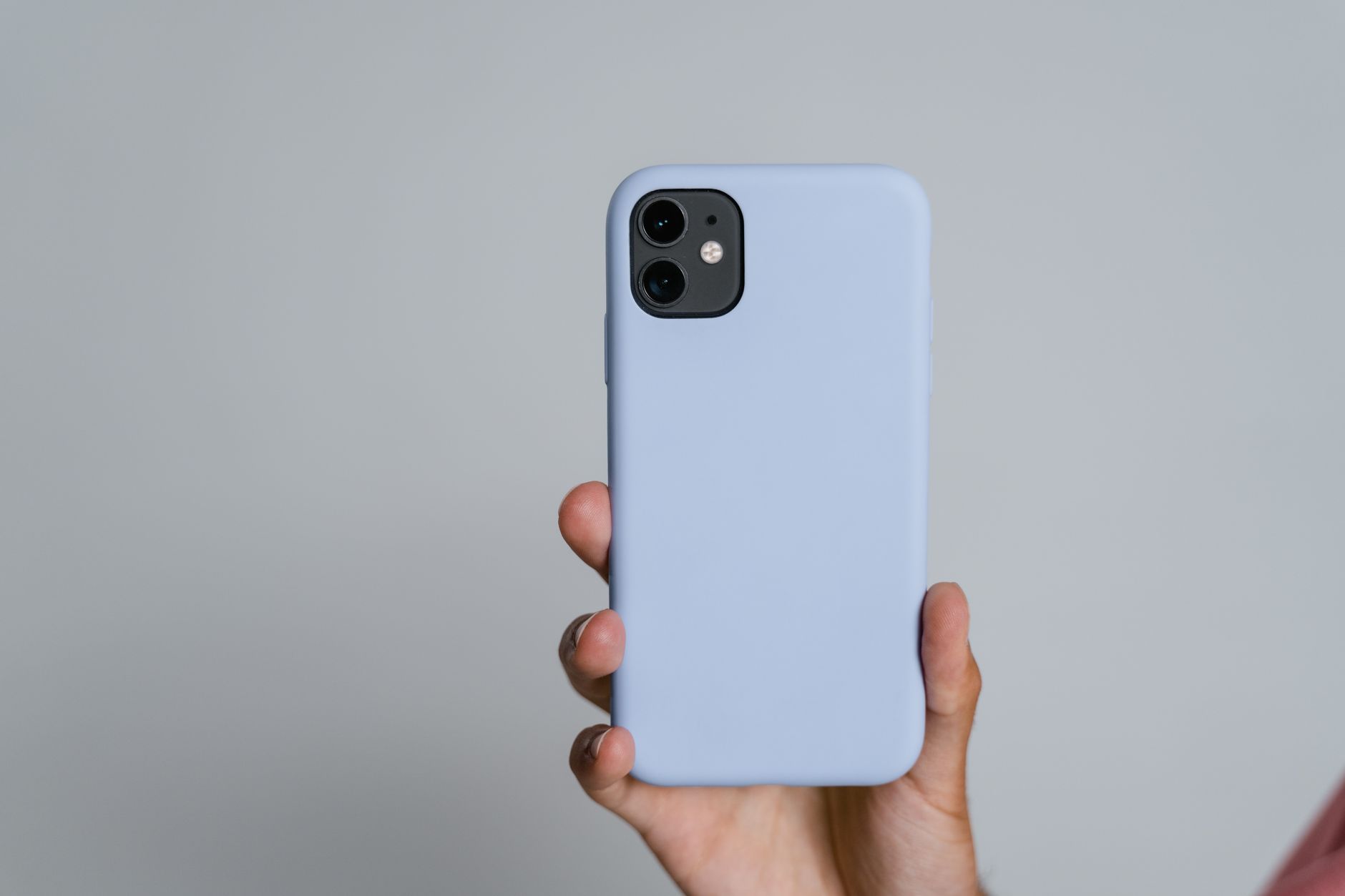 Lyseblå smartphone med dobbelt kamera holdt i hånden mod neutral baggrund.