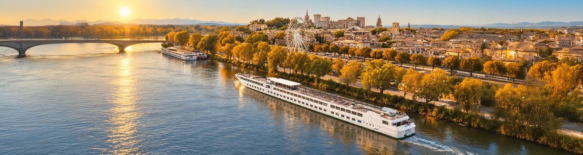 Bateau de croisière fluviale naviguant sur fleuve au coucher de soleil avec ville et cathédrale en arrière-plan